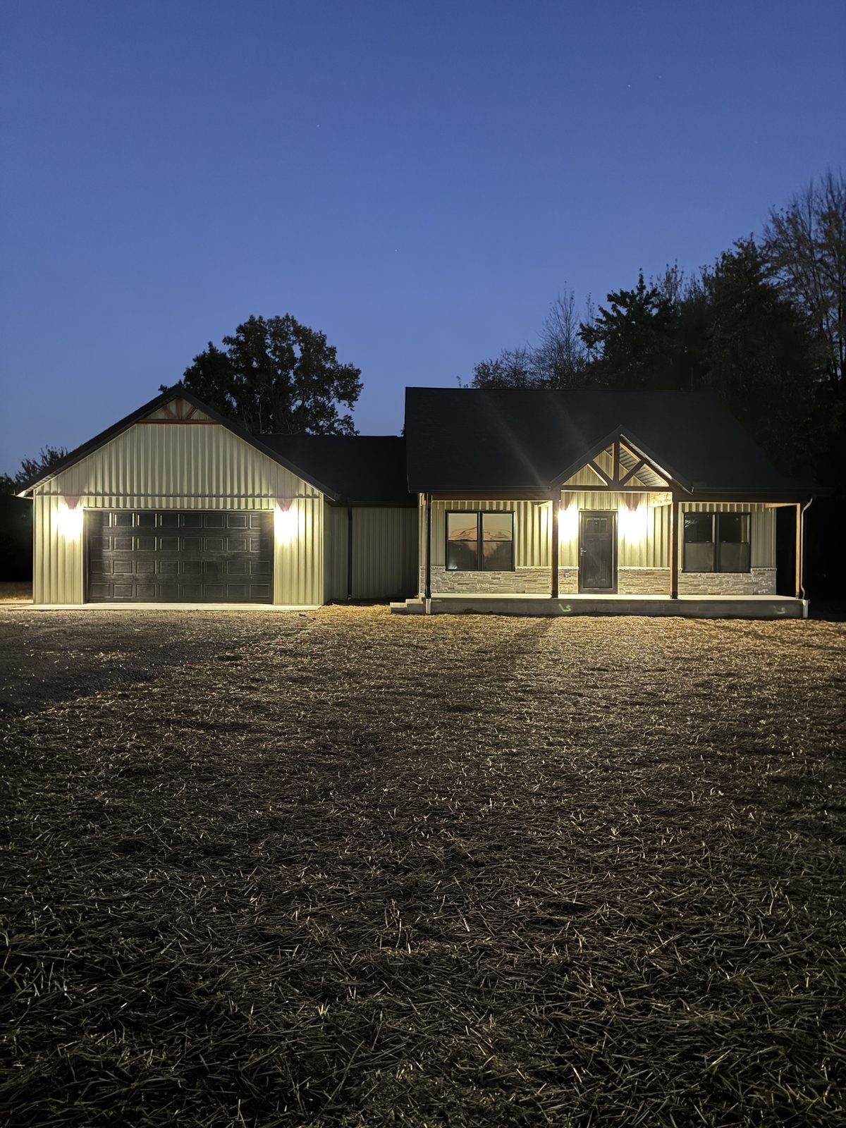 Stonebrook — SID-built home at dusk with lit front porch, timber gable accent and two-car garage